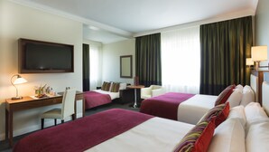 A hotel room with two beds, a desk, a chair, a TV, and a window with curtains.