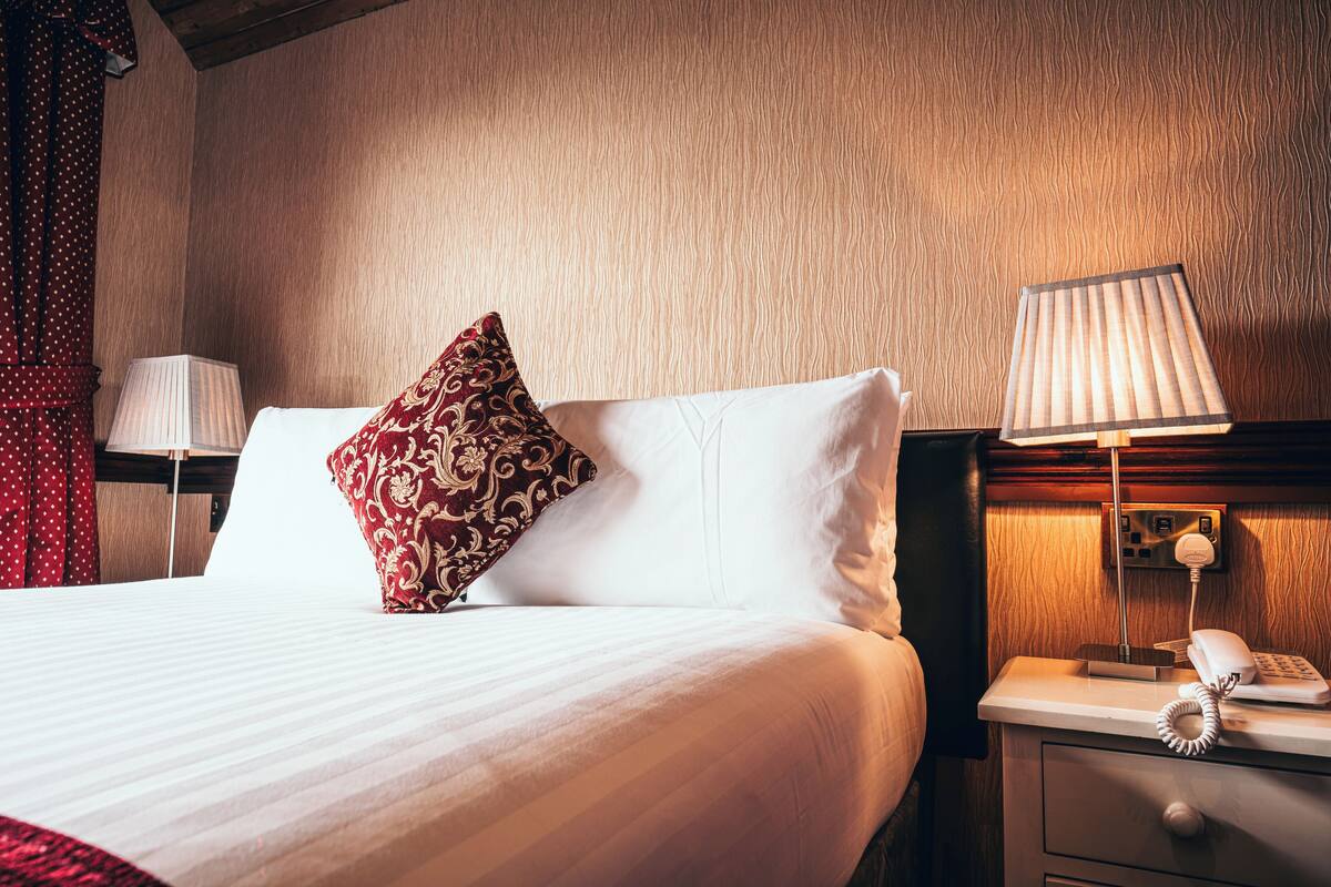 A neatly made bed with a patterned pillow, a bedside lamp, and a phone on a wooden nightstand.