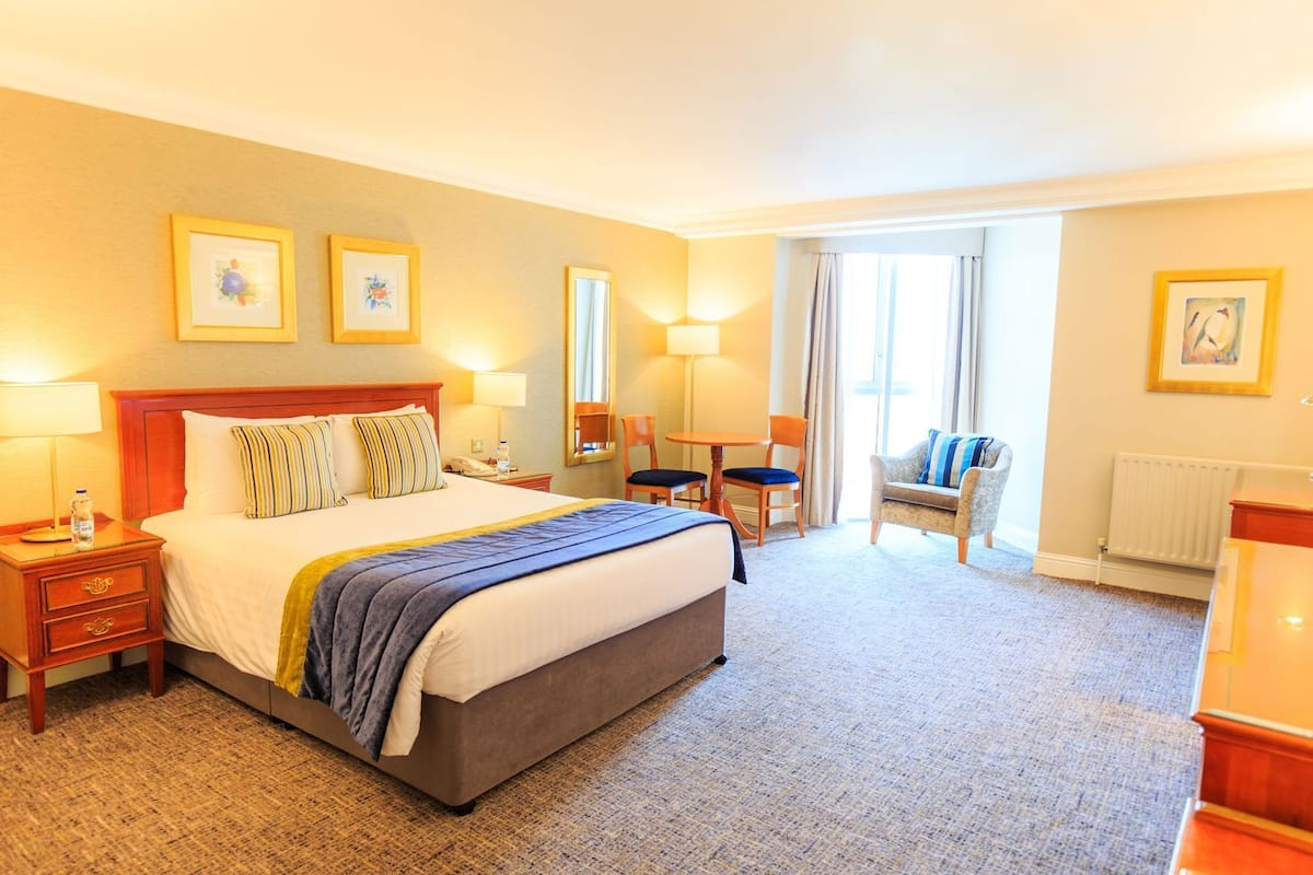 A hotel room with a bed, bedside tables, a chair, a small table, and a radiator.