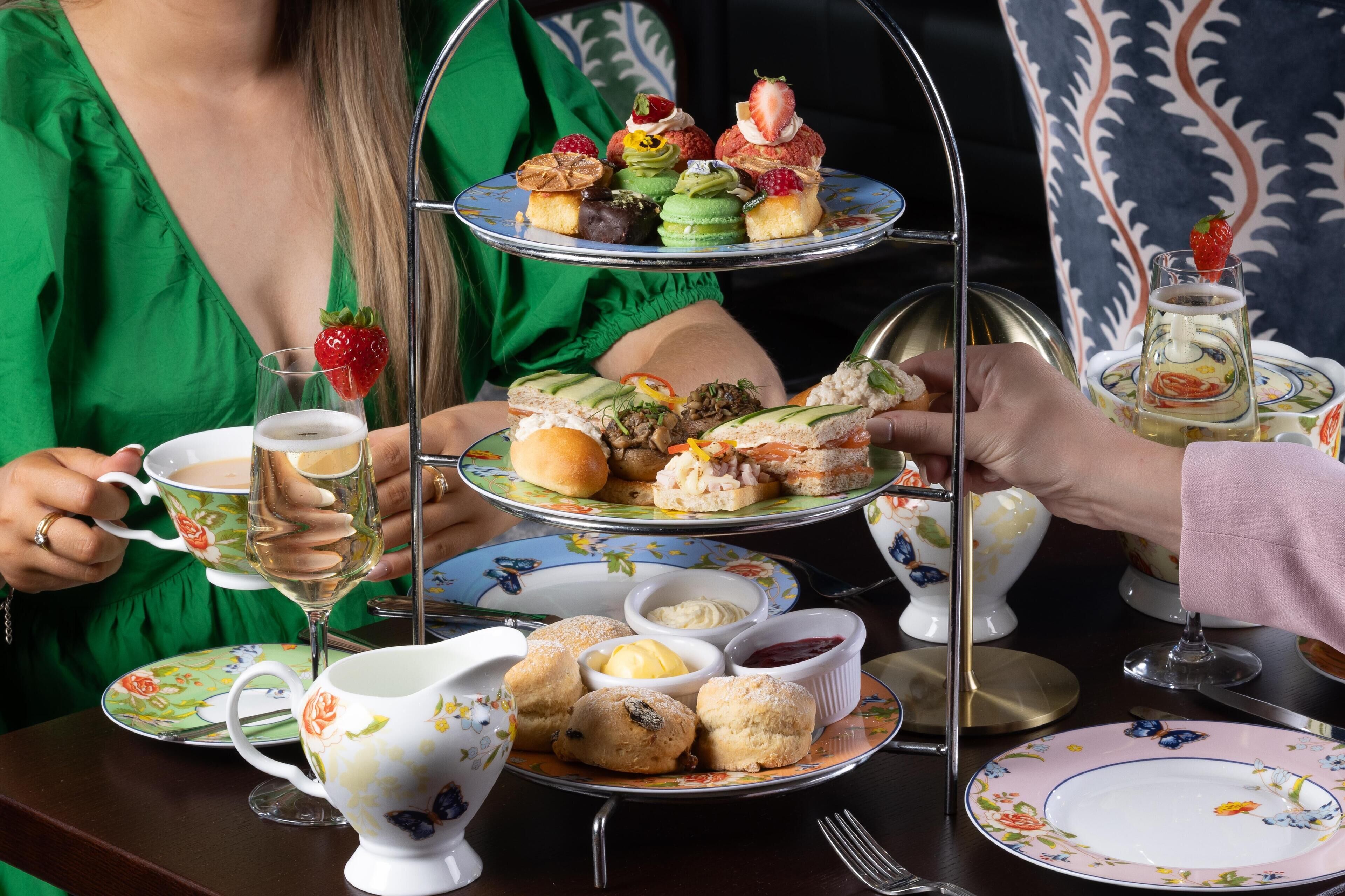 Servicio de té en varios niveles con pasteles, scones, una tetera y una taza de té.
