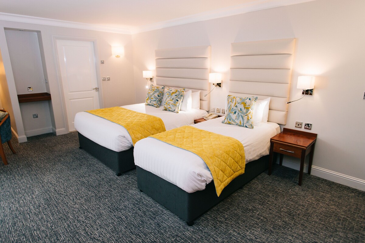 Habitación de hotel con dos camas, una mesita de noche y una puerta.