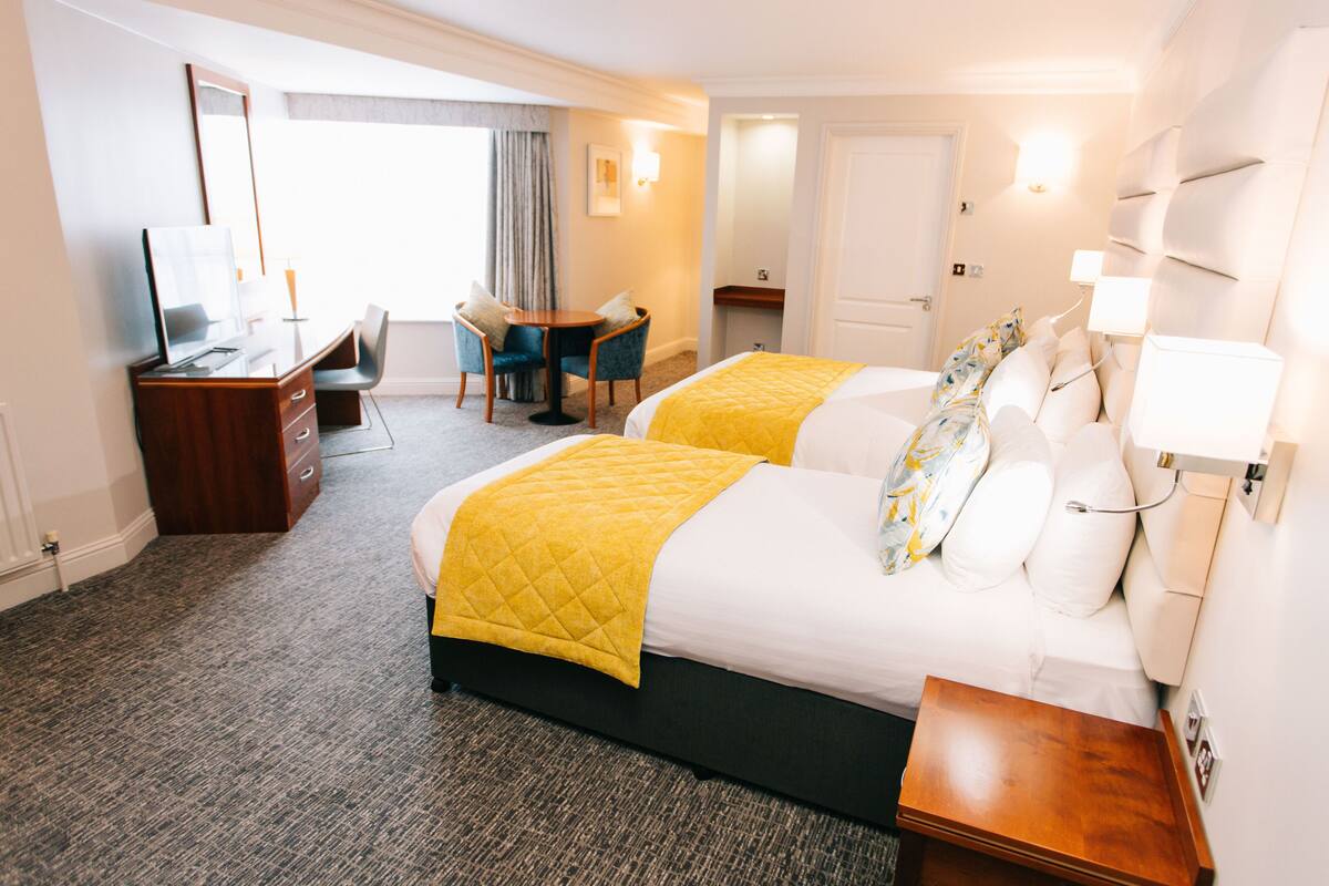 A hotel room with two beds, a desk, a chair, a small table, and a TV.