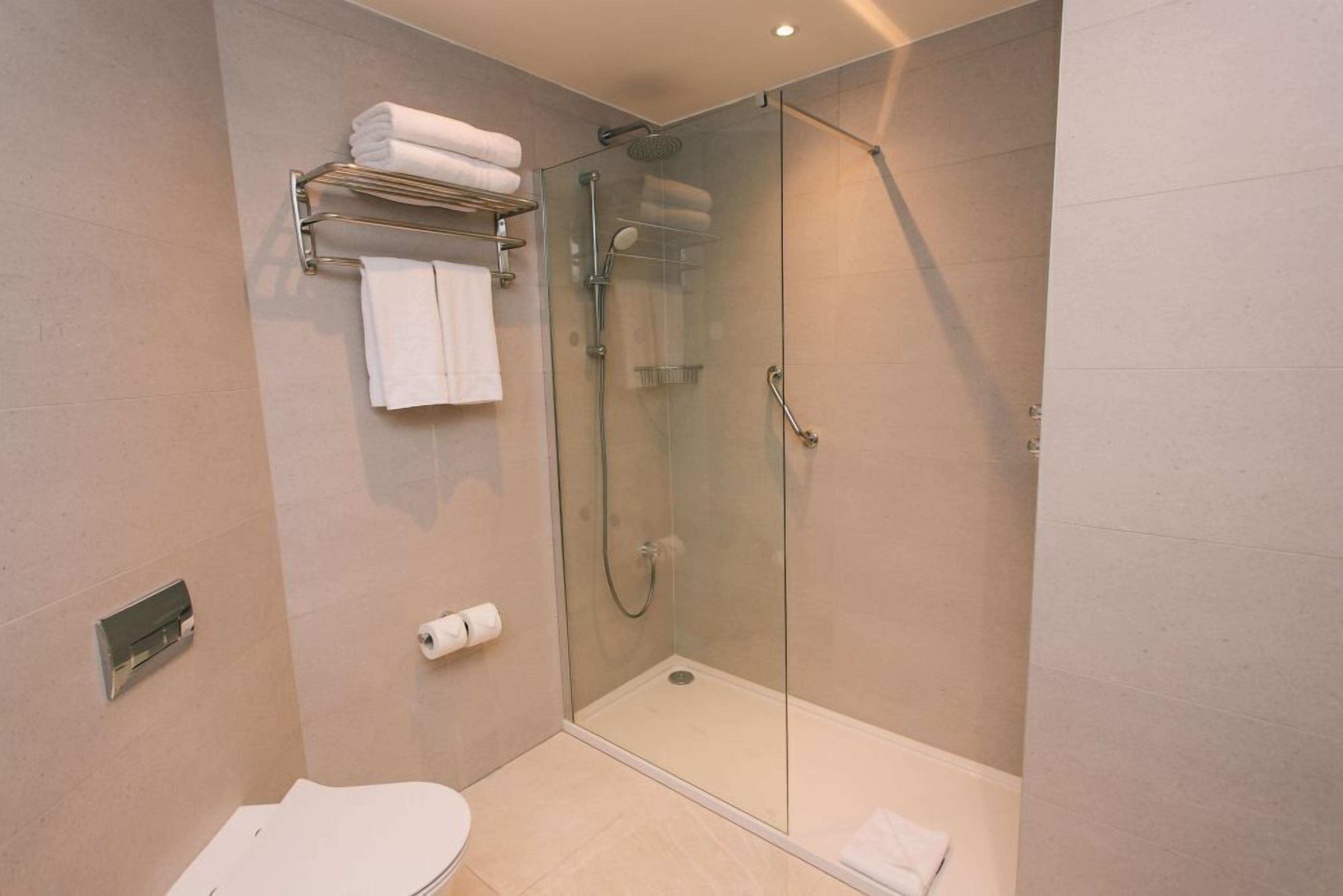A modern bathroom with a glass-enclosed shower, a toilet, and a towel rack.