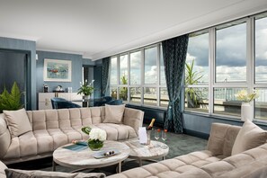 A modern living room with a large window, a sofa set, a coffee table, and a view of the city. - Grand Hotel (Malahide)