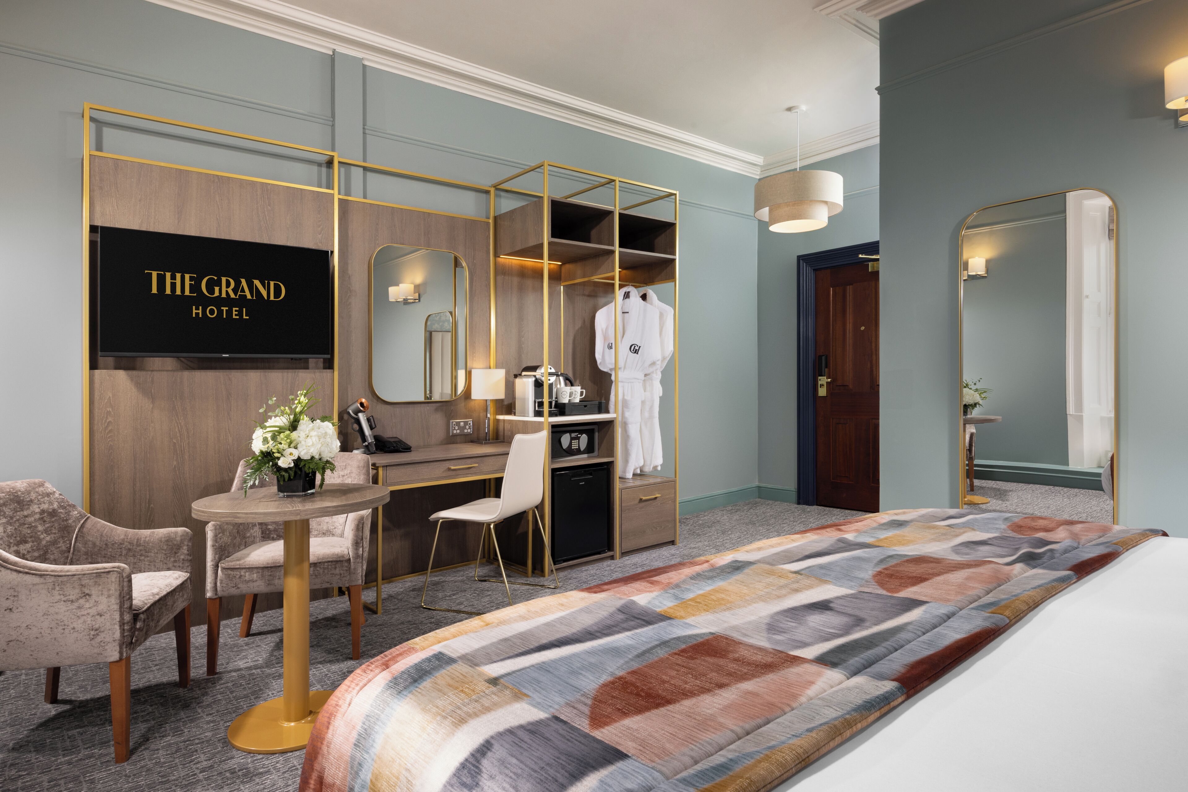 A hotel room with a bed, a desk, a chair, a small table, a mirror, and a wardrobe.