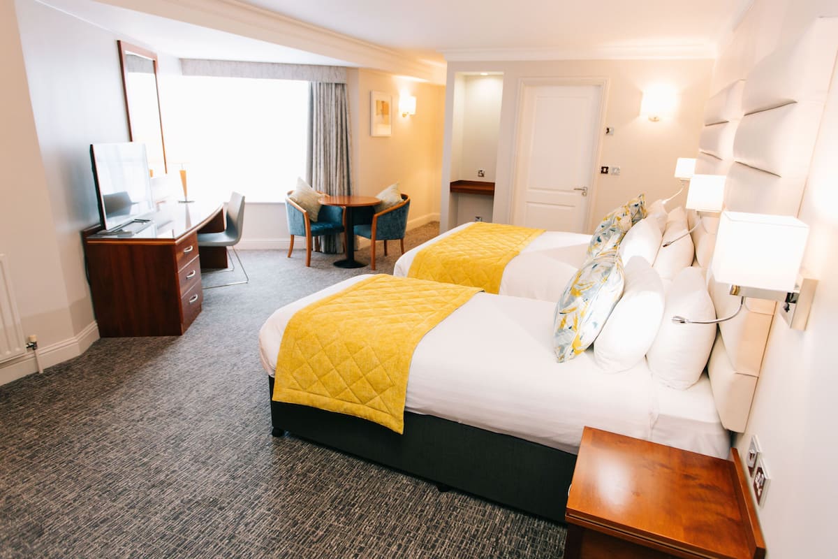 A hotel room with two beds, a desk, a chair, a small table, and a mirror.