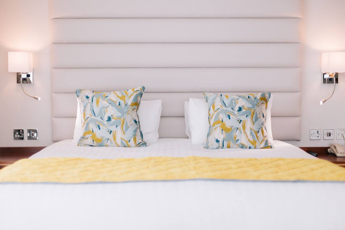 A hotel room with a large bed, two decorative pillows, bedside lamps, and a telephone on the nightstand.
