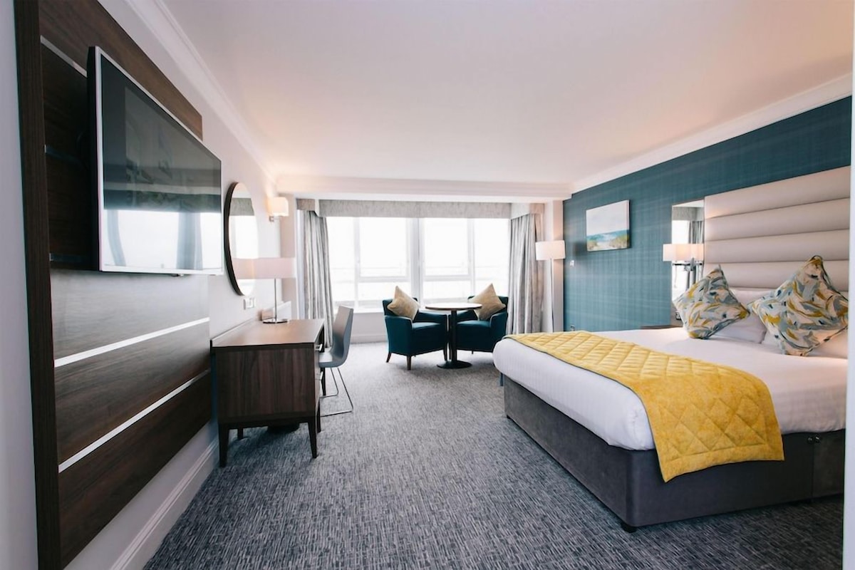 Una habitación de hotel con cama, escritorio, silla, televisor y ventana.
