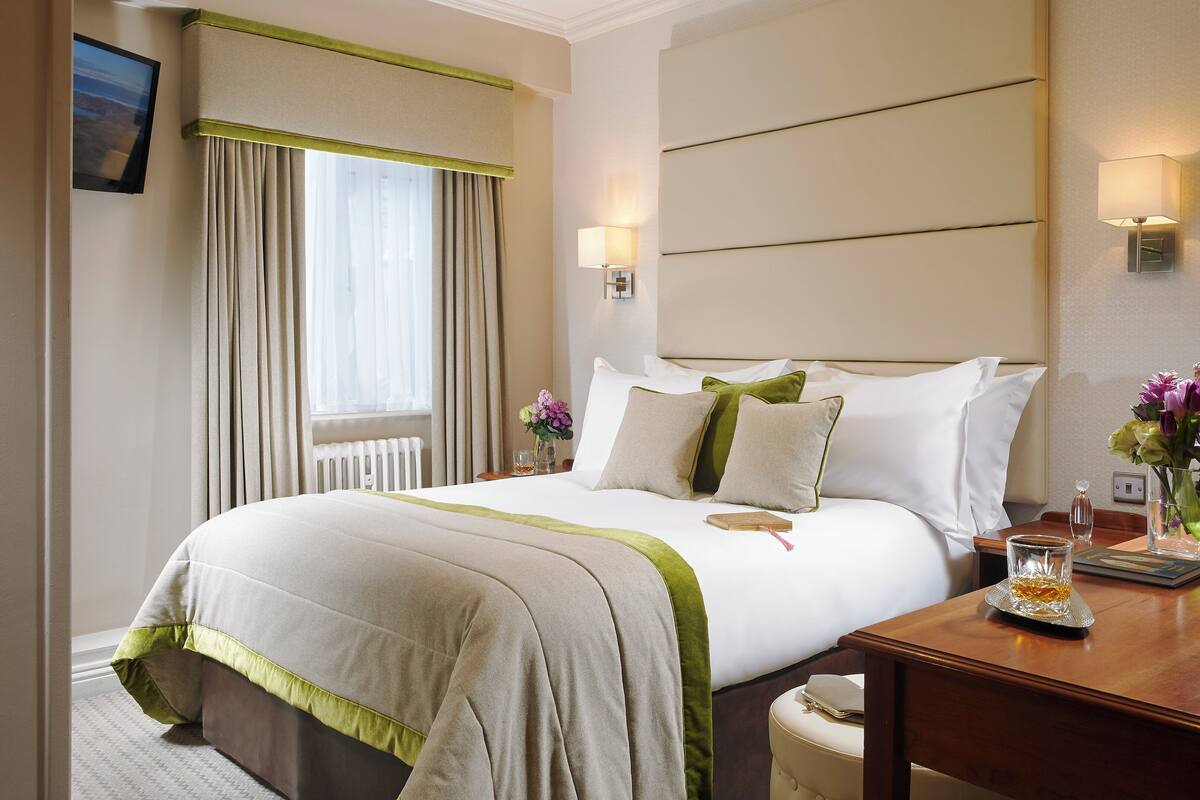 Una habitación de hotel con una cama grande, una mesita de noche, una lámpara y una ventana con cortinas.