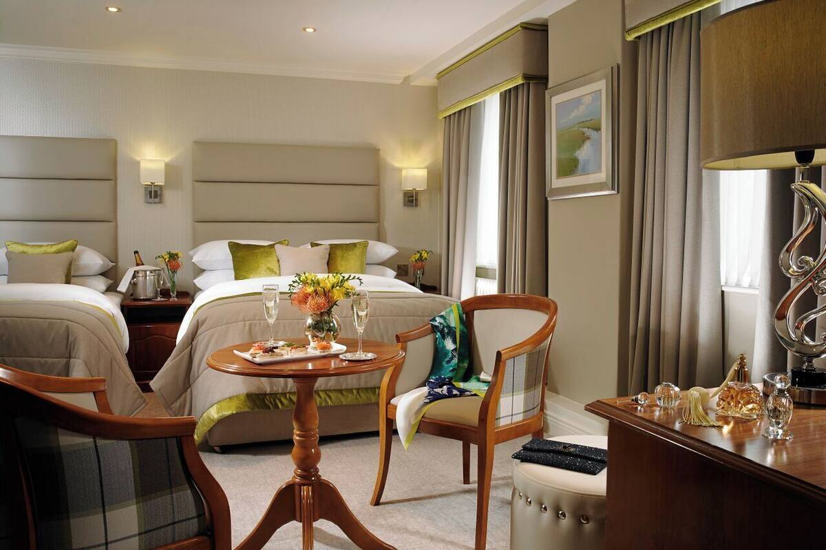 Una habitación de hotel con dos camas, una mesa de comedor con un florero, una silla y un escritorio con una lámpara y objetos decorativos.