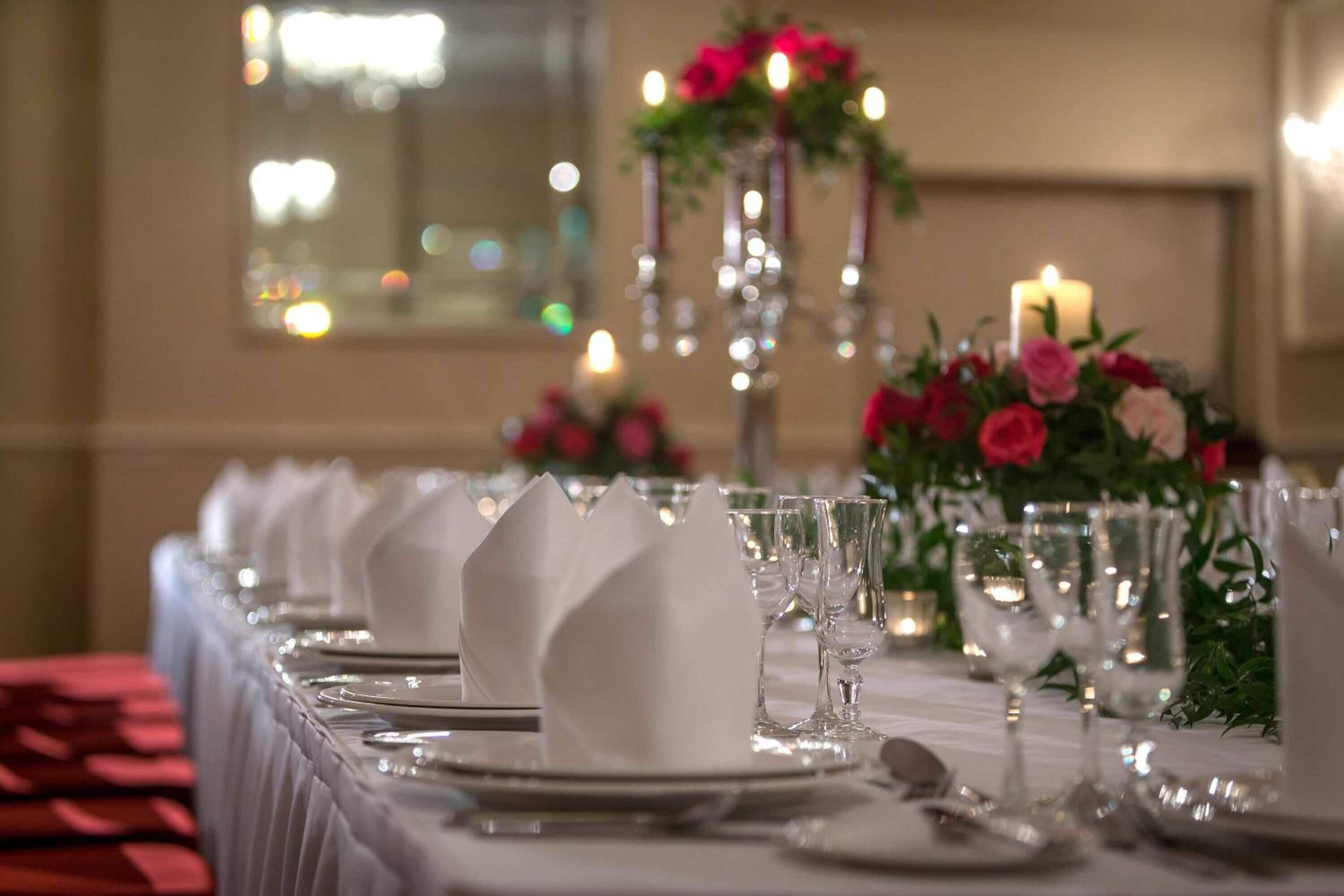 A long dining table set with white napkins, plates, and clear glassware, adorned with a floral centerpiece and candles.