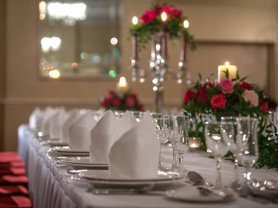 A long dining table set with white napkins, plates, and clear glassware, adorned with a floral centerpiece and candles.