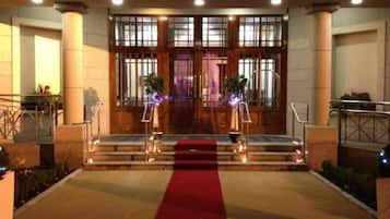 Ingresso di un hotel con tappeto rosso, doppie porte e una scala che sale.