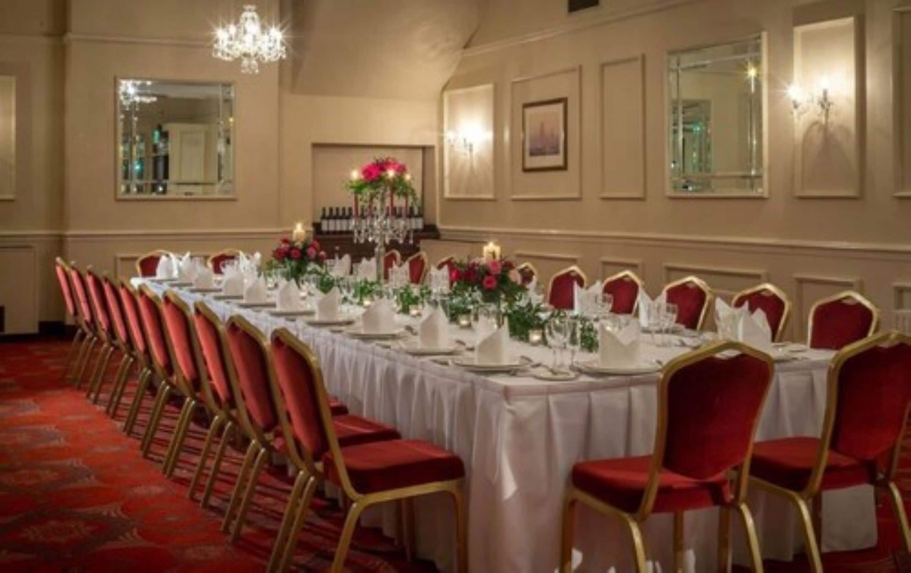 A long banquet table set with white tablecloths, red chairs, and floral centerpieces.