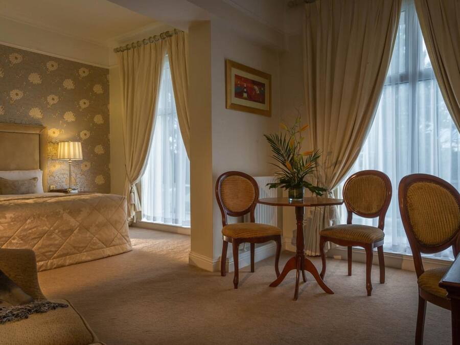 Una habitación de hotel con cama, zona de estar con mesa y sillas, lámpara y un cuadro en la pared.