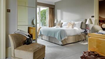 A hotel room with a large bed, a sitting area with a chair, a desk, and a view of greenery outside.