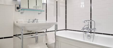 A modern bathroom with a white sink, chrome fixtures, a glass shelf, and a bathtub.