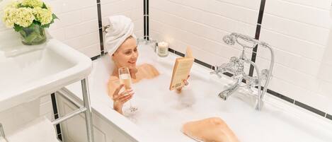 A person in a bathtub with a book and a glass of wine.