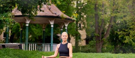 Una persona meditando sobre una esterilla en un parque con un pabellón al fondo.