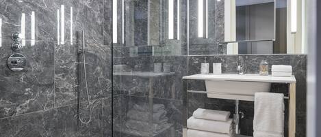 Un baño moderno con ducha de vidrio, paredes de mármol y tocador con espejo y toallero.