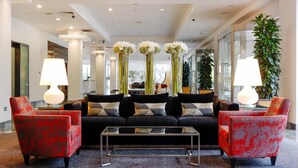 A modern lobby with a black sofa, red armchairs, a glass coffee table, and white lamps. - Herbert Park Hotel (Dublin)