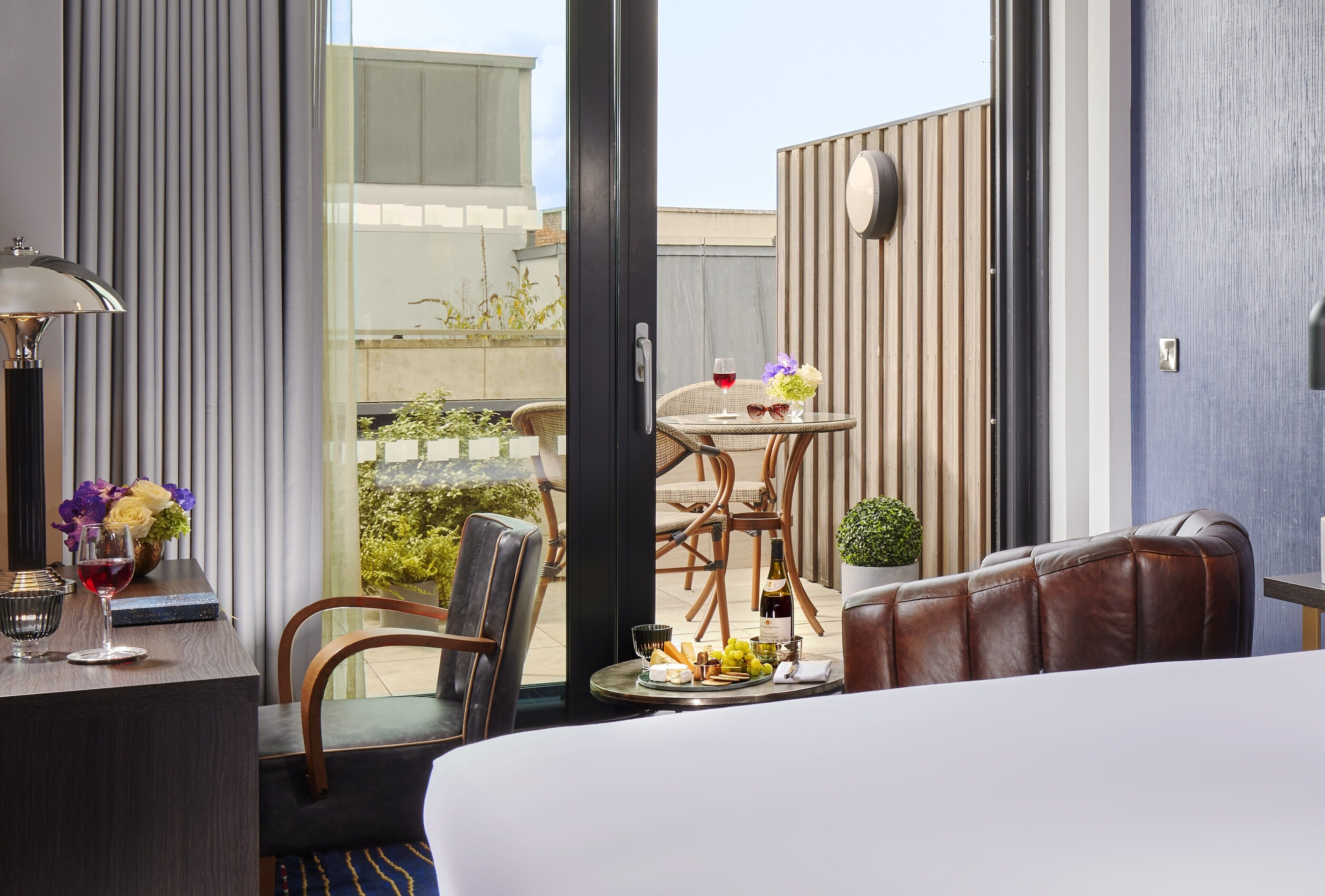 A hotel room with a bed, a sitting area with a table, chairs, and a view of the outside.