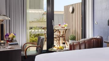 A hotel room with a bed, a sitting area with a table, chairs, and a view of the outside.