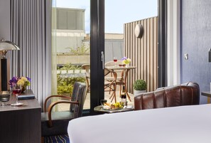 A hotel room with a bed, a sitting area with a table, chairs, and a view of the outside. - The Grafton Hotel (Dublin)