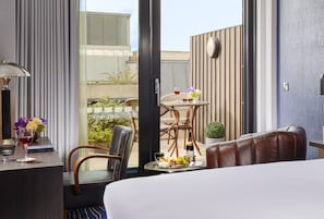 A hotel room with a bed, a sitting area with a table, chairs, and a view of the outside.