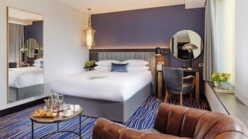 A hotel room with a large bed, a desk, a chair, a coffee table, and a leather armchair.