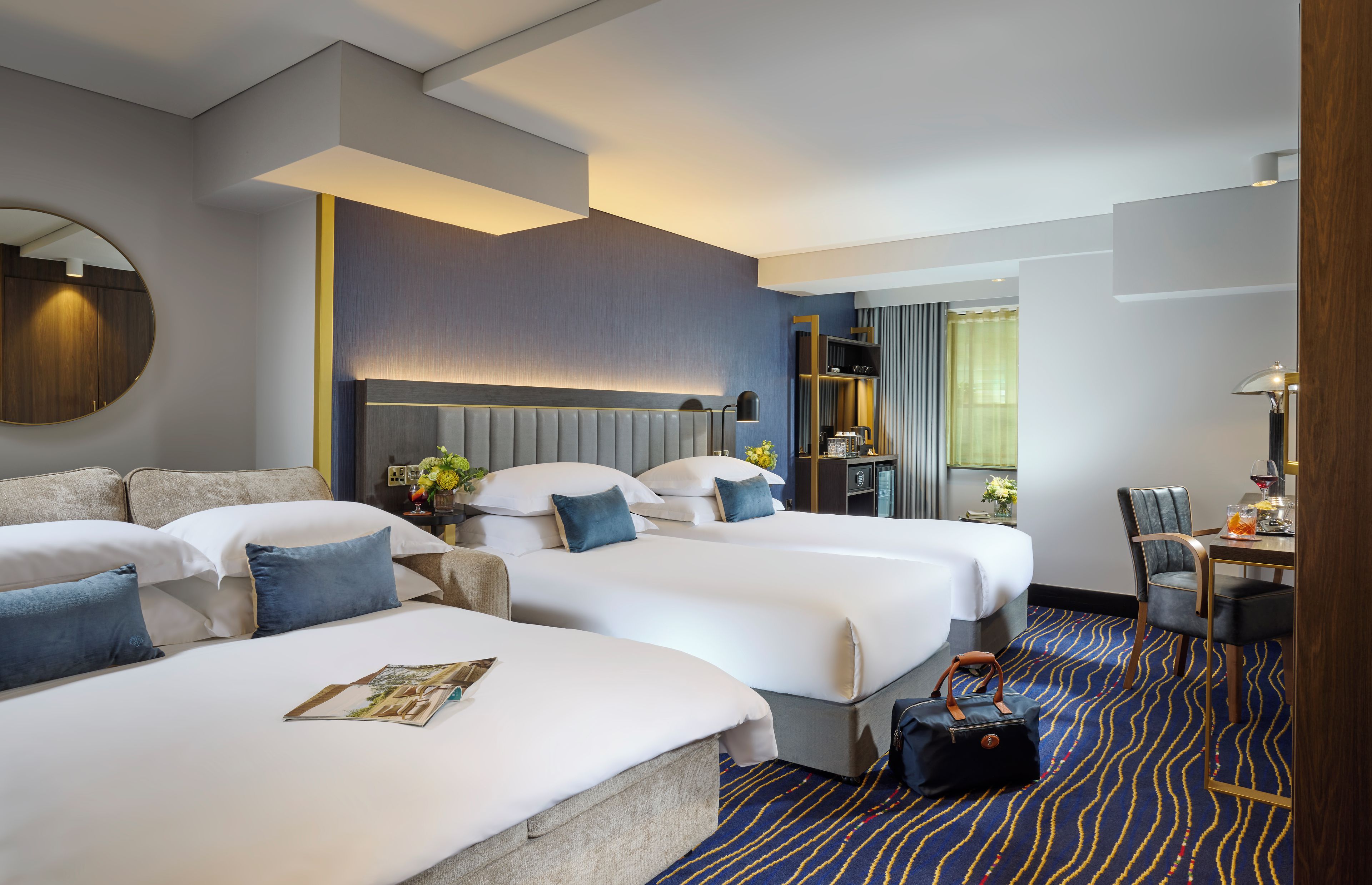 A hotel room with two beds, a desk, a chair, a mirror, and a window with curtains.