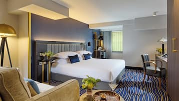Una habitación de hotel con una cama grande, un escritorio, una silla, una lámpara y una mesita con un florero y una bandeja.