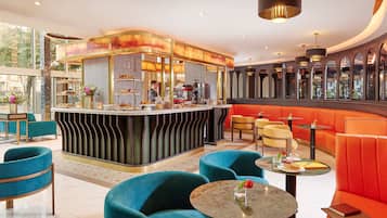 A modern hotel lobby with a central bar area, seating arrangements, and a view through large windows.