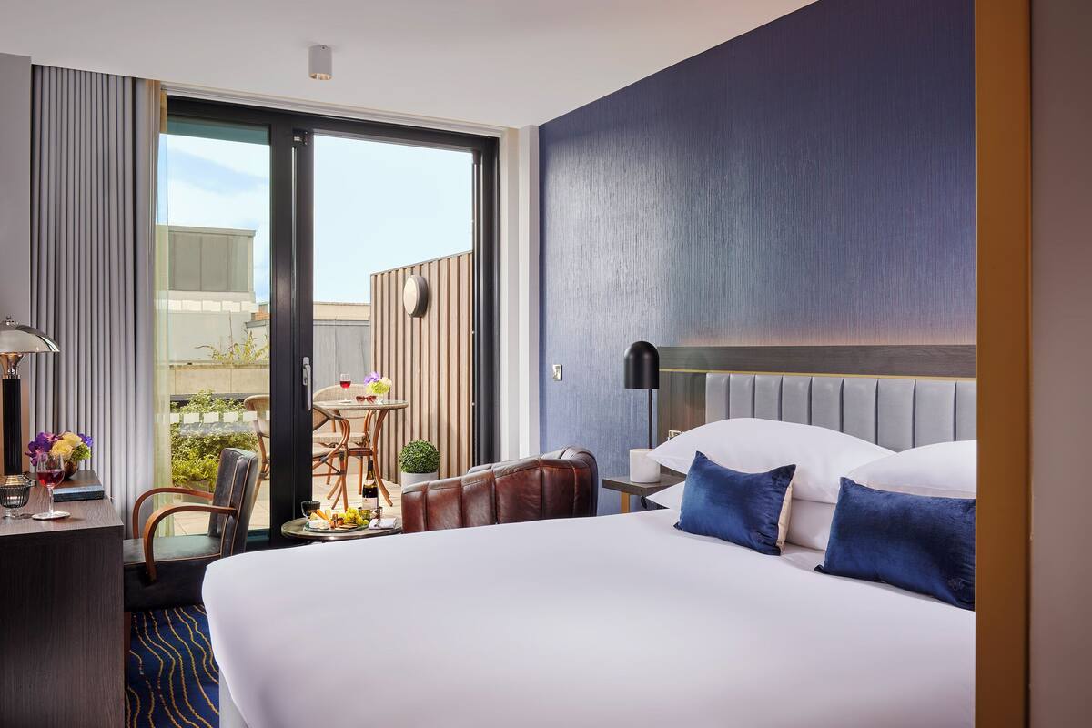 A hotel room with a large bed, a desk with a lamp, a chair, and a view of the outdoors.