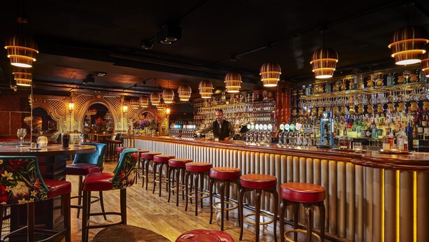 A bar with a bartender, wooden bar stools, and a variety of bottles and glasses on shelves. - The Grafton Hotel (Dublin)