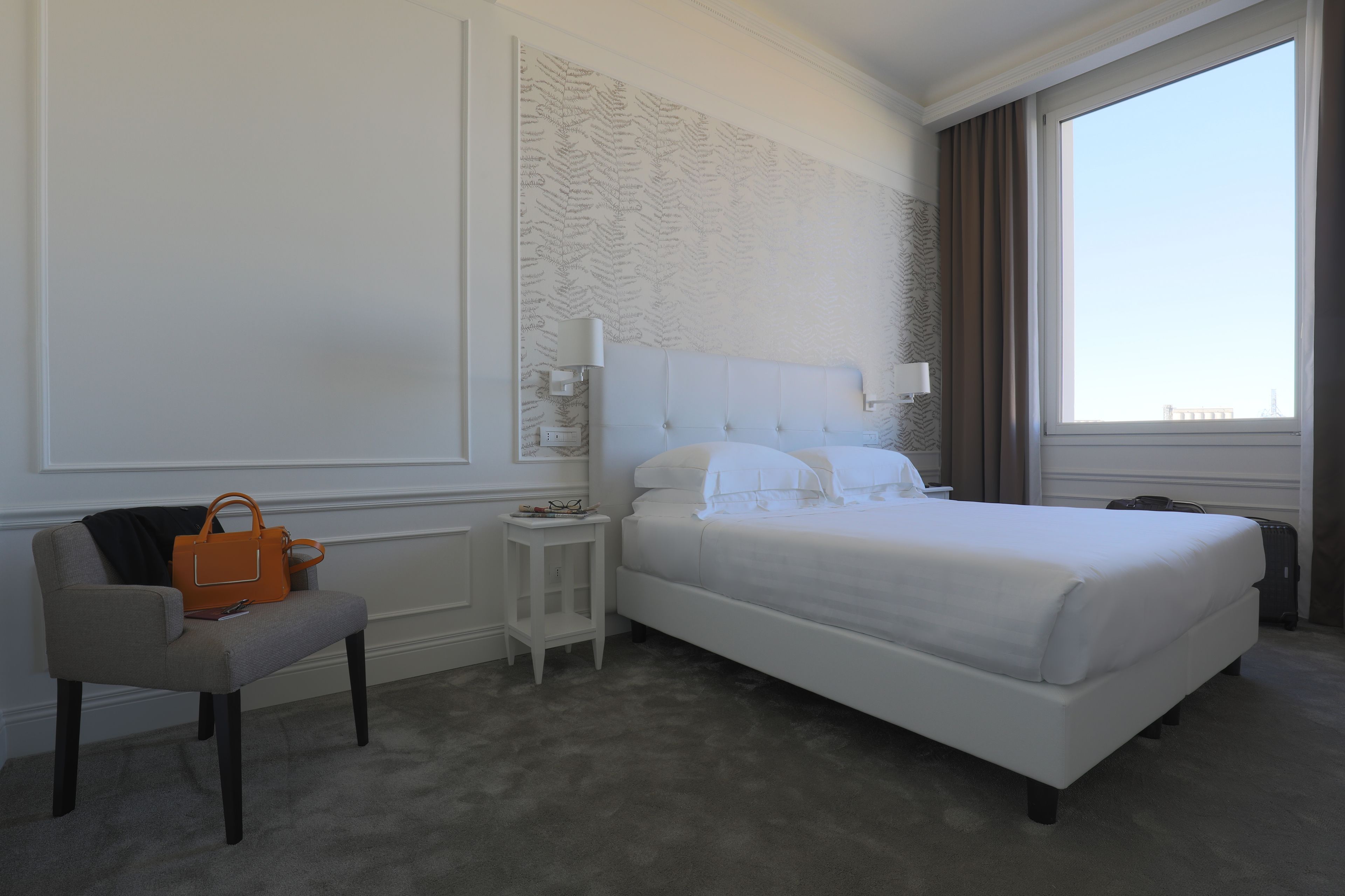 Una habitación de hotel con una cama grande, una silla, una mesita y una ventana con cortinas.