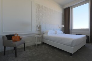 Una habitación de hotel con una cama grande, una silla, una mesita y una ventana con cortinas.