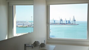Een badkamer met een groot raam met uitzicht op een haven, een wastafel en een spiegel.