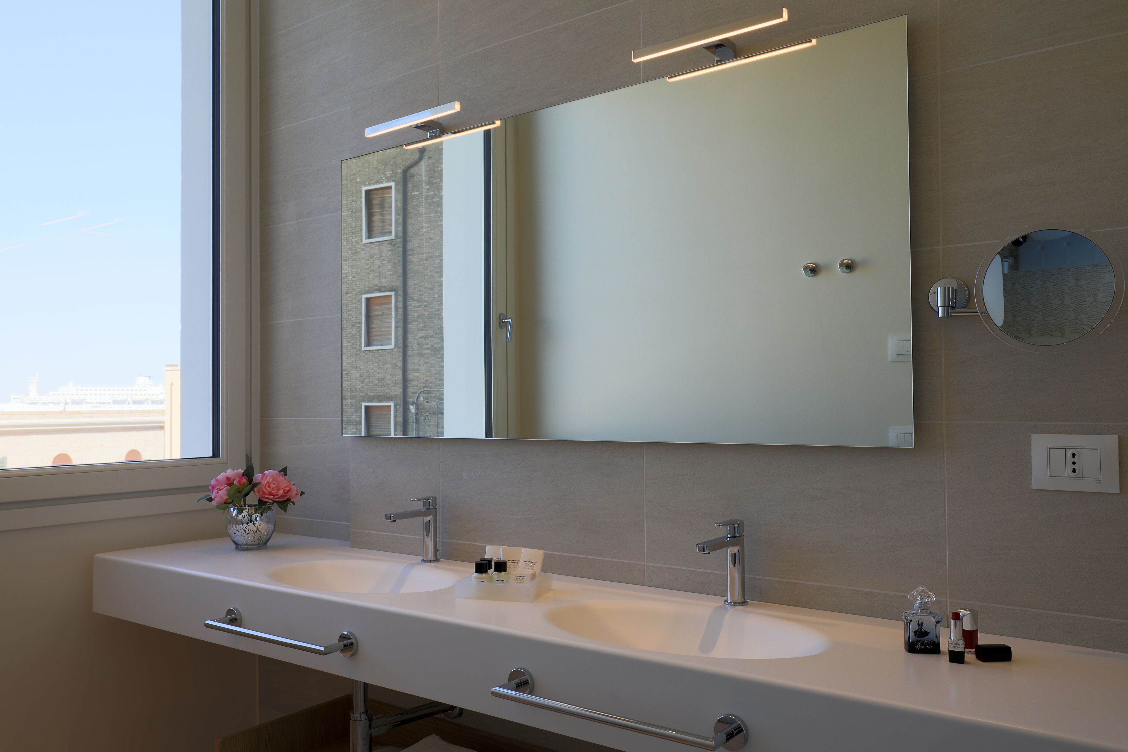 Un baño moderno con dos lavamanos, un espejo grande y un florero con flores.