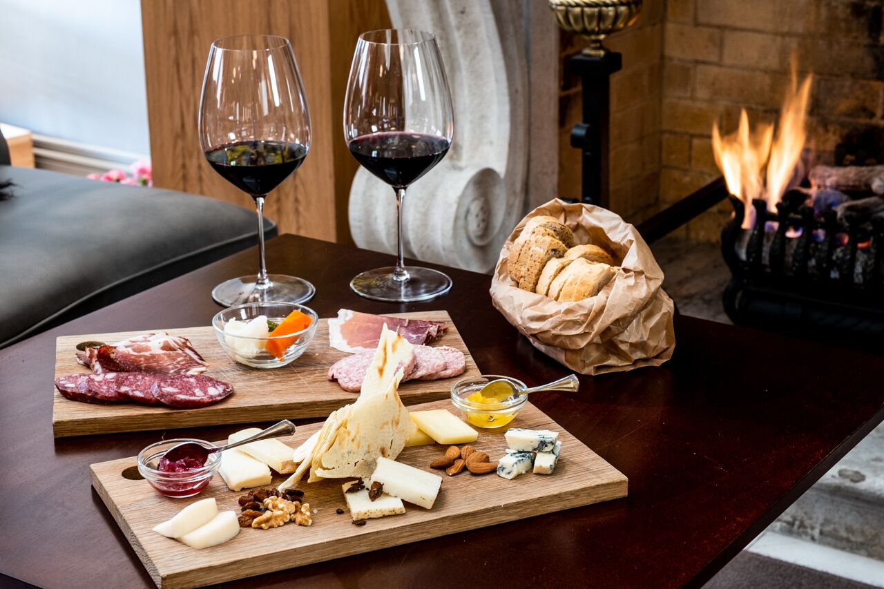 A wooden table with a charcuterie board, two glasses of red wine, and a basket of bread.