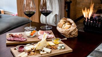 A wooden table with a charcuterie board, two glasses of red wine, and a basket of bread.