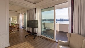 Een ruime woonkamer met een grote flatscreen-tv, een eethoek met een houten tafel en stoelen, en een balkon met uitzicht op een stadsbeeld en water.