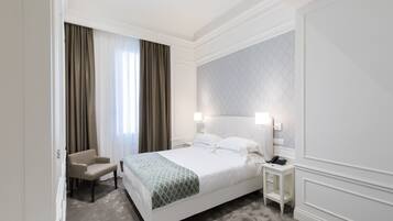 Camera d'albergo con un letto grande, una sedia, un comodino con il telefono e una finestra con tende.
