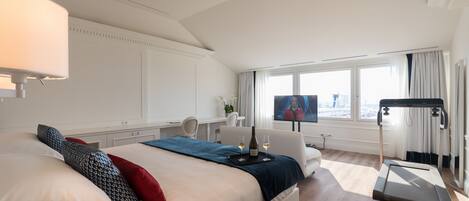 A modern hotel room with a large bed, a treadmill, a desk with a chair, and a TV.