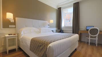 A hotel room with a large bed, bedside tables, a desk with a chair, and a window with curtains.