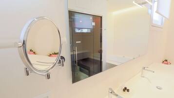 A modern bathroom with a large mirror, a glass-enclosed shower, and a vanity with a sink and countertop.