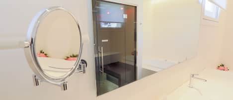 A modern bathroom with a large mirror, a glass-enclosed shower, and a vanity with a sink and countertop.