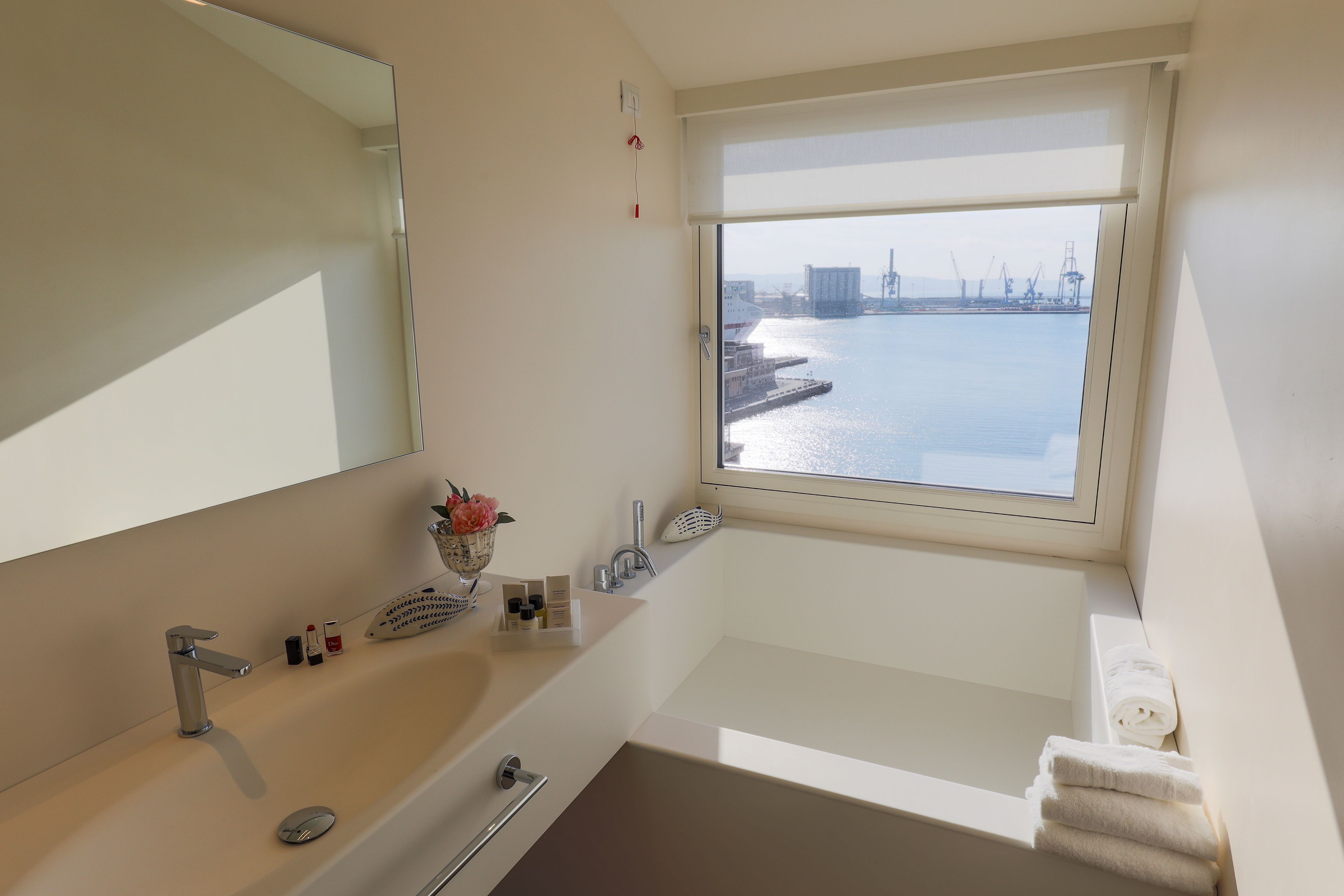 A modern bathroom with a large window, a bathtub, a sink, and a mirror.