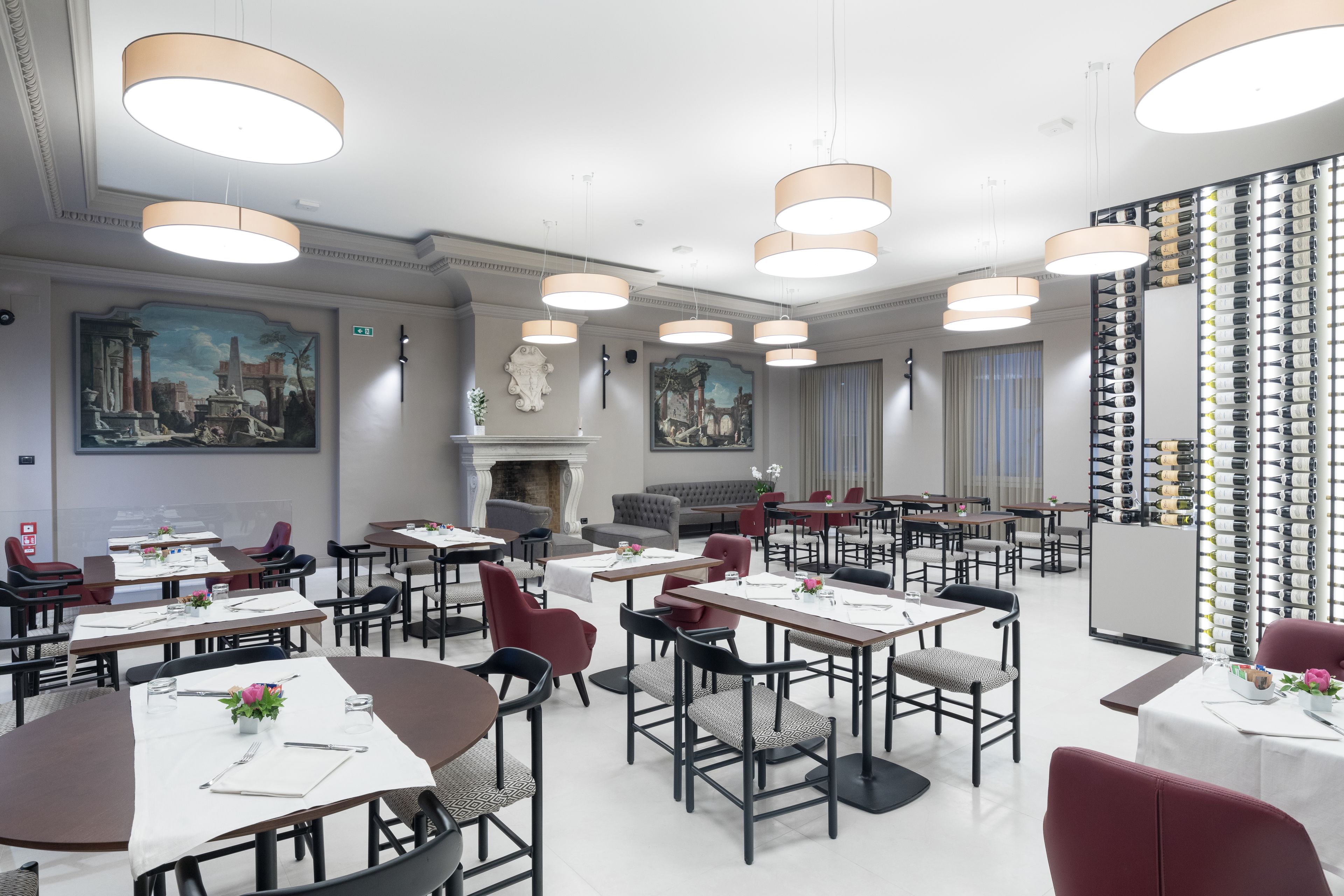 A spacious dining area with multiple tables and chairs, a fireplace, and a wall of wine bottles.