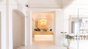 Een receptie met een kroonluchter, een receptiebalie en een bord met de tekst 'Grand Hotel Palace'.